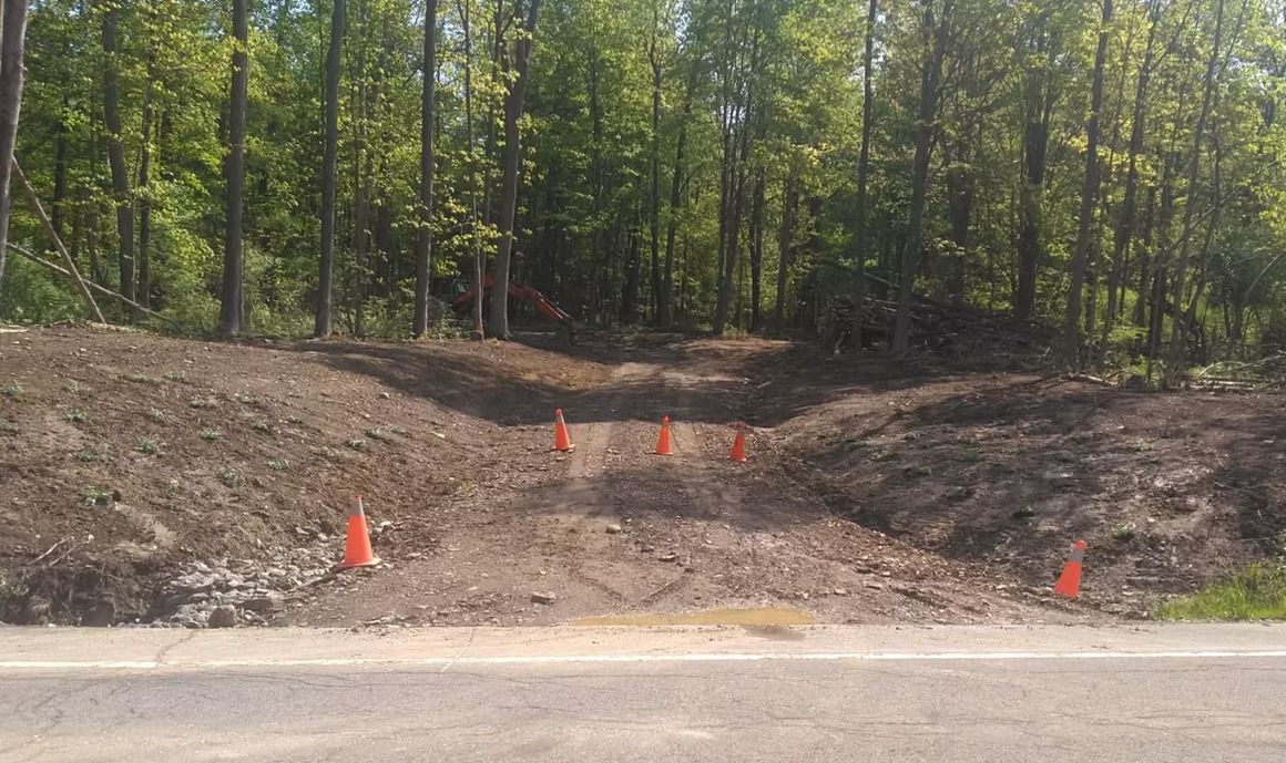 Landmark Enterprises site preparation in Chautauqua County, NY — new driveway cut off the road marked with safety cones and an excavator on site